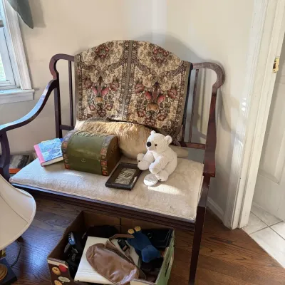 Sale Photo Thumbnail #64: Vintage dark wood bench with an upholstered seat, decorated with a patterned throw, plush polar bear, and small green box.
