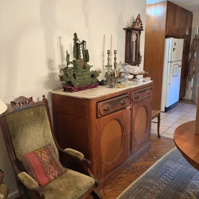 Sale Photo Thumbnail #105: Antique carved wooden sideboard with marble top, accompanied by a green velvet platform rocker and various decorative tabletop items.
