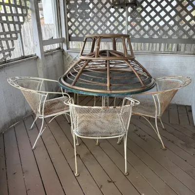 Sale Photo Thumbnail #104: Vintage wrought iron outdoor dining set with four expanded metal chairs, a round table, and a tiered bamboo base resting on top.