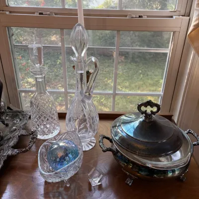 Sale Photo Thumbnail #24: Collection of tabletop decor including crystal decanters, a glass bowl with a blue decorative orb, a silver-plated tray, and a silver-plated chafing dish.