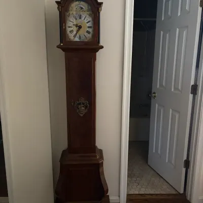 Sale Photo Thumbnail #70: Traditional wooden grandfather clock featuring a bonnet top, decorative metal accents on the body, and an ornate clock face with Roman numerals.