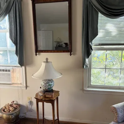 Sale Photo Thumbnail #58: Traditional Chippendale-style mahogany wall mirror with an ornate fretwork pediment, paired with a small wooden accent table and porcelain table lamp.