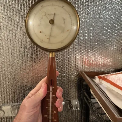 Sale Photo Thumbnail #101: Vintage mid-century modern weather instrument combining a circular brass barometer with a wooden handle thermometer.