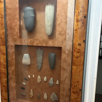 Sale Photo Thumbnail #31: Framed shadow box display of Native American stone artifacts, including stone axe heads, celts, and various projectile points, presented in a burled wood frame.