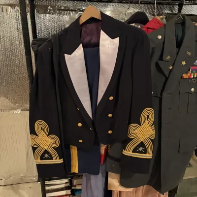 Sale Photo Thumbnail #100: Vintage U.S. Army mess dress jacket with ornate gold sleeve braid and crossed cannons infantry insignia, displayed alongside a green service uniform coat on a clothing rack.