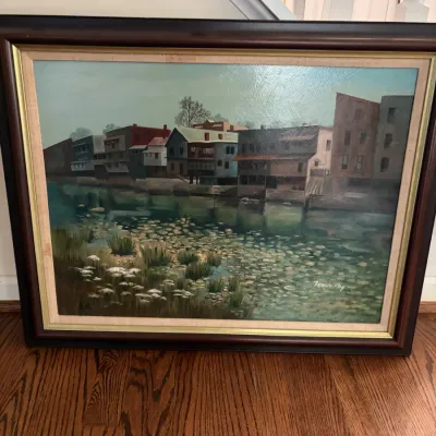 Sale Photo Thumbnail #10: Framed oil painting depicting a waterfront town scene with buildings along a canal, signed by the artist in the lower right.