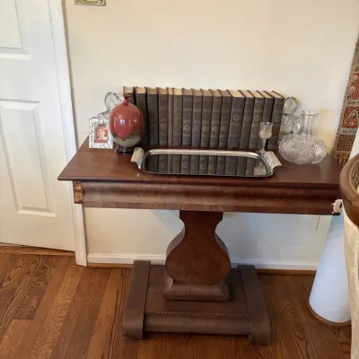 Sale Photo Thumbnail #18: Antique mahogany flip-top game table with a central pedestal base, displaying a collection of vintage hardbound books, a silver-plated tray, crystal glassware, and decorative accents.