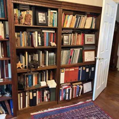 Sale Photo Thumbnail #93: Pair of traditional dark wood tall bookcases filled with books, framed photos, and decor, set above an Oriental area rug.