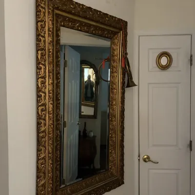 Sale Photo Thumbnail #69: Large ornate giltwood wall mirror with detailed scrollwork frame, mounted alongside a brass hunting horn.