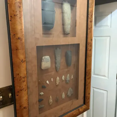 Sale Photo Thumbnail #30: Framed shadowbox display featuring a collection of Native American artifacts, including stone axe heads, celts, and arrowheads, housed in a burl wood frame.