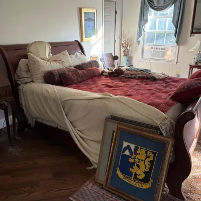 Sale Photo Thumbnail #65: Traditional wooden sleigh bed dressed with patterned linens and decorative pillows, accompanied by framed wall art leaning against the footboard.