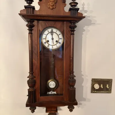 Sale Photo Thumbnail #41: Antique Vienna regulator-style wall clock in a carved walnut case with decorative finials and a carved mask pediment detail.