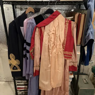 Sale Photo Thumbnail #99: Collection of vintage costumes and ceremonial garments hanging on a wire rack alongside books and storage boxes.