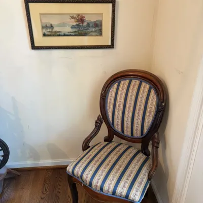Sale Photo Thumbnail #20: Victorian-style carved wood armchair with blue and beige striped floral upholstery, positioned below a framed landscape art print.