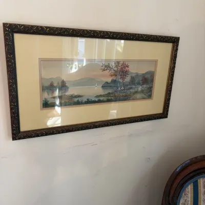 Sale Photo Thumbnail #115: Framed panoramic watercolor painting depicting a scenic lake landscape with mountains and a sailboat, presented in a matted dark ornate frame.