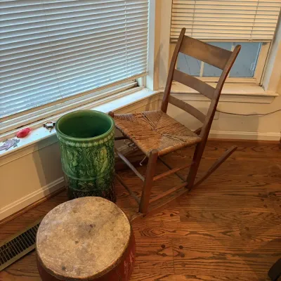 Sale Photo Thumbnail #53: Vintage ladderback rocking chair with a woven rush seat alongside a green glazed ceramic umbrella stand and a round wooden drum-style stool.