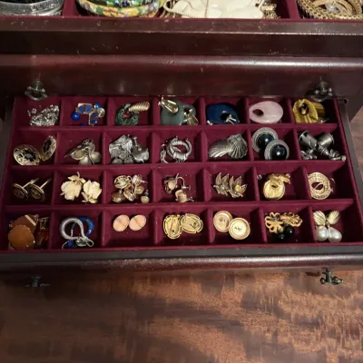 Sale Photo Thumbnail #83: Wooden jewelry chest filled with vintage costume jewelry, including various clip-on and stud earrings, bangles, and necklaces in plush burgundy compartments.