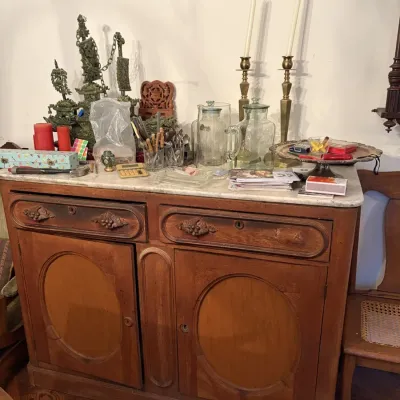 Sale Photo Thumbnail #40: Antique carved wooden sideboard with marble top, featuring carved drawer pulls and oval door panels, holding various vintage glassware, candlesticks, and decorative smalls.