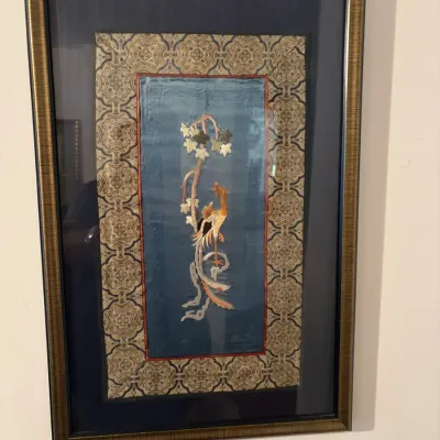 Sale Photo Thumbnail #79: Framed Chinese silk embroidery sleeve panel featuring a detailed phoenix and floral motif on blue silk, mounted with a patterned fabric border in a metallic gold frame.