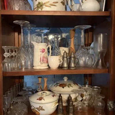 Sale Photo Thumbnail #37: Wooden display cabinet filled with vintage tableware, including crystal stemware, silver-toned salt and pepper shakers, and ceramic serving dishes with floral and fruit motifs.