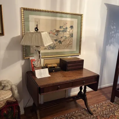 Sale Photo Thumbnail #77: Traditional wooden drop-leaf sofa table or writing desk with turned legs, displaying decorative boxes, a cut glass lamp, and a large framed Asian art print hanging above.