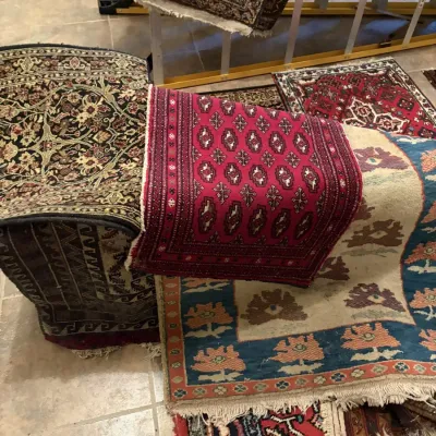 Sale Photo Thumbnail #112: A collection of hand-woven area rugs and runners in various traditional Persian and Oriental patterns, displayed over a rack and on the floor.