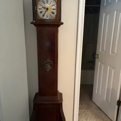 Sale Photo Thumbnail #127: Vintage dark wood grandfather clock featuring an ornate brass dial with Roman numerals and decorative brass accents.