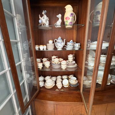 Sale Photo Thumbnail #25: Mid-century wooden china cabinet with open glass doors, filled with delicate porcelain teacups, saucers, and decorative figurines.