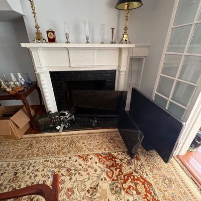 Sale Photo Thumbnail #23: Collection of electronics including flat-screen televisions and a portable boombox resting near a fireplace hearth, surrounded by brass lamps, glassware, and an oriental area rug.