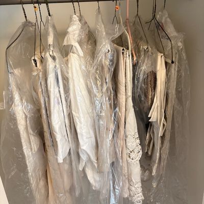 Sale Photo Thumbnail #8: Assorted white and off-white vintage garments hanging in clear plastic garment bags on wire hangers inside a closet.