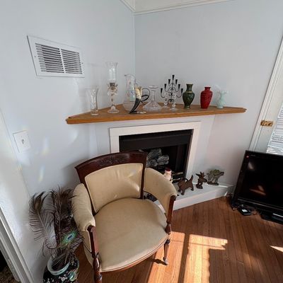 Sale Photo Thumbnail #36: Vintage wood-framed barrel chair with beige upholstery set in front of a corner fireplace mantel displaying decorative glassware, vases, and candelabras.