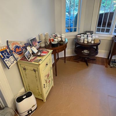 Sale Photo Thumbnail #45: A light yellow floral hand-painted accent cabinet, a wood drop-leaf table, and a round tiered table displaying ceramic coffee mugs, sports pennants, and small decor.