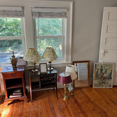 Sale Photo Thumbnail #10: Selection of vintage furniture and decor, including brass and ceramic table lamps with pleated shades, a dark wood nightstand and wine rack table, a rectangular wall mirror, and framed artwork.