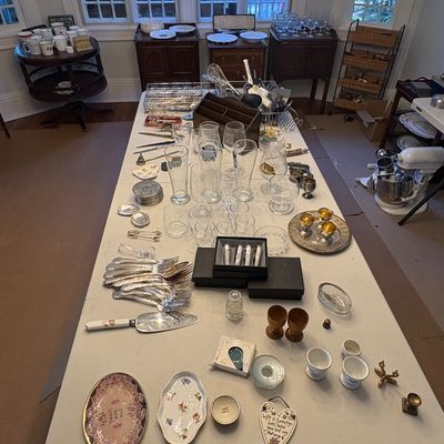 Sale Photo Thumbnail #44: Large folding table displayed with a variety of household goods including glassware, silver-plated flatware, decorative trinkets, and small serving pieces.