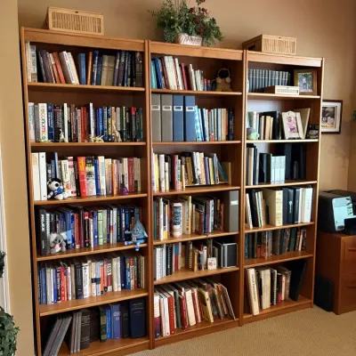 Set of three matching light oak wood tall bookcases filled with a variety of books, office binders, and decorative items.