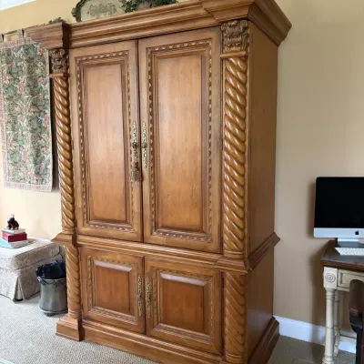 Large wooden armoire featuring twisted rope-style column details, carved accents, decorative brass hardware, and two double-door cabinet...