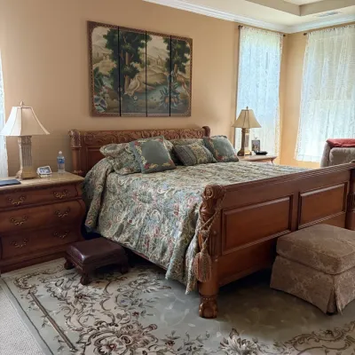 Ornately carved wooden sleigh bed set with matching nightstands, a triptych wall painting, and a large patterned area rug.