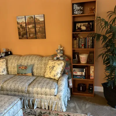 Traditional blue and white patterned sofa with ruffled skirt, paired with a matching ottoman, three-piece landscape canvas art, and a...