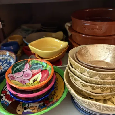 Collection of decorative ceramic bowls and terra cotta dishes arranged inside a cabinet, featuring hand-painted Mexican pottery and...