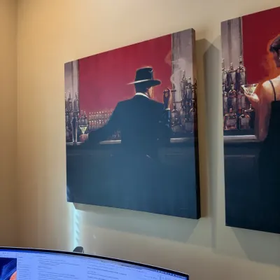Large canvas print featuring a noir-style scene of a man in a hat smoking at a bar, mounted on a wall alongside a matching piece.