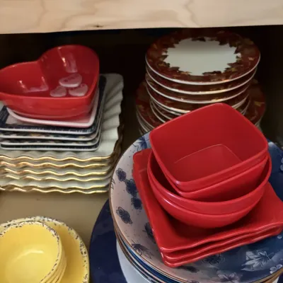 An assortment of colorful ceramic dishware including red bowls, yellow speckled bowls, square red bowls, and various patterned plates...