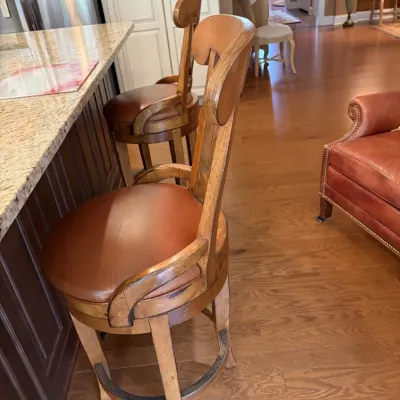 Pair of traditional wooden swivel barstools featuring contoured backs, curved armrests, and brown leather upholstered seats.