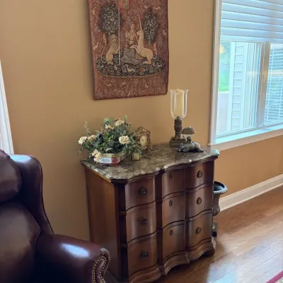 Serpentine front wood chest with a marble top, accompanied by a medieval-style unicorn wall tapestry and tabletop decor.