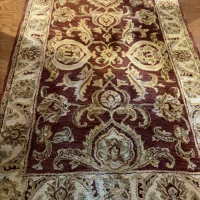Hand-tufted wool area rug featuring a traditional ornate floral scroll motif in burgundy, beige, and sage green shades.
