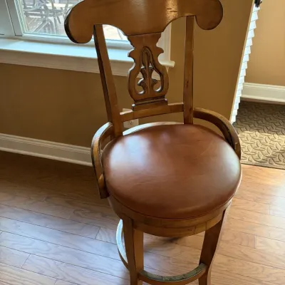 Traditional wooden swivel bar stool featuring a carved backrest with a decorative crest, curved arm supports, and a round brown...