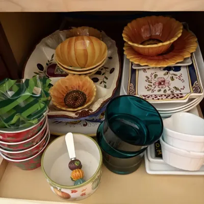 Assorted tableware and serving pieces, including floral and pumpkin-themed bowls, hand-painted platters, and teal glass cups.