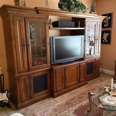 Large wooden entertainment center with leaded glass doors and lower cabinet storage, housing a flat-screen television.