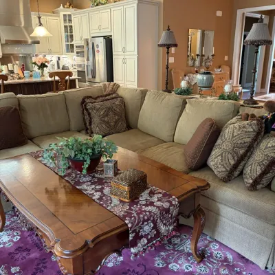 Large beige L-shaped sectional sofa paired with an ornate carved wood coffee table and matching throw pillows in a traditional living area.