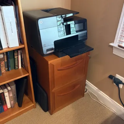 Black HP Officejet all-in-one printer resting on a two-drawer wooden filing cabinet.