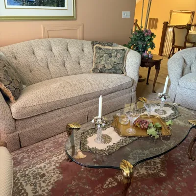 Traditional living room set featuring a tufted camelback sofa with patterned upholstery, a matching armchair, and a glass-top coffee...